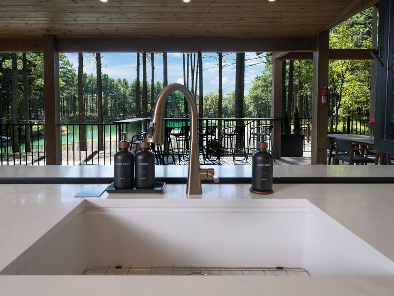 Stylish farmhouse-style kitchen sink with a brushed-gold faucet, featuring views of the wooded property