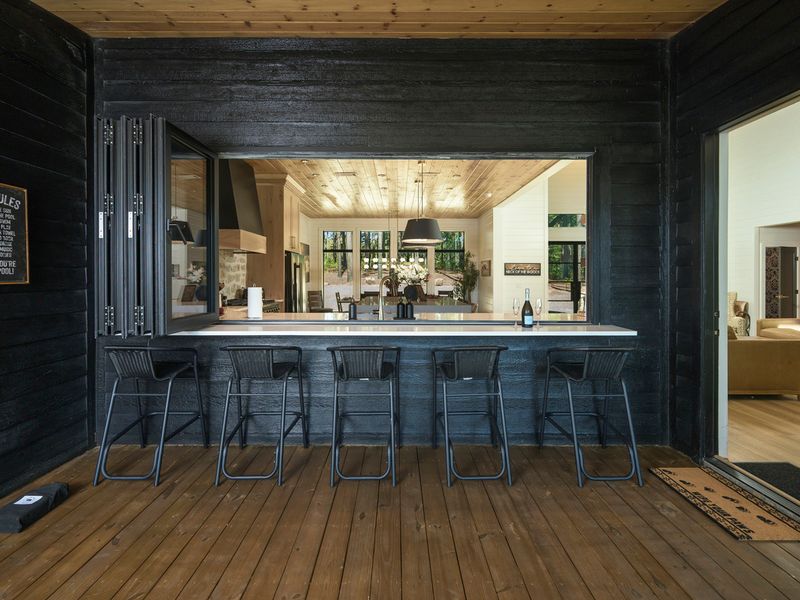 Stylish outdoor bar area with black stools, seamlessly connecting to a modern chef's kitchen, ideal