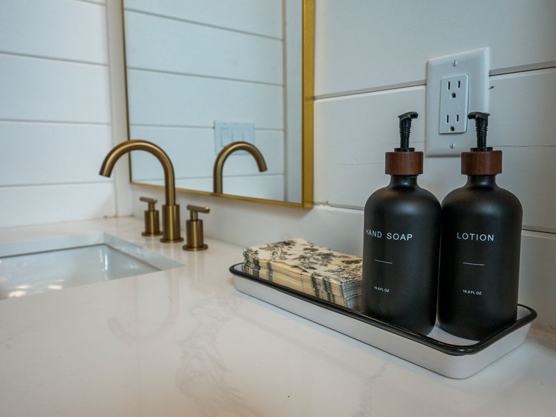 Elegant vanity with gold fixtures, a large mirror, and complimentary hand soap and lotion.