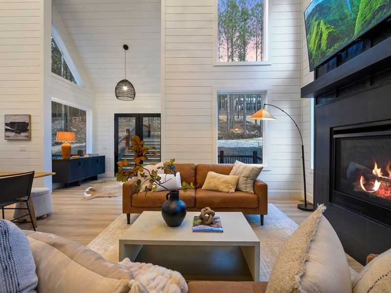 Soaring ceilings and dramatic windows create a bright, open living space surrounded by forest views.
