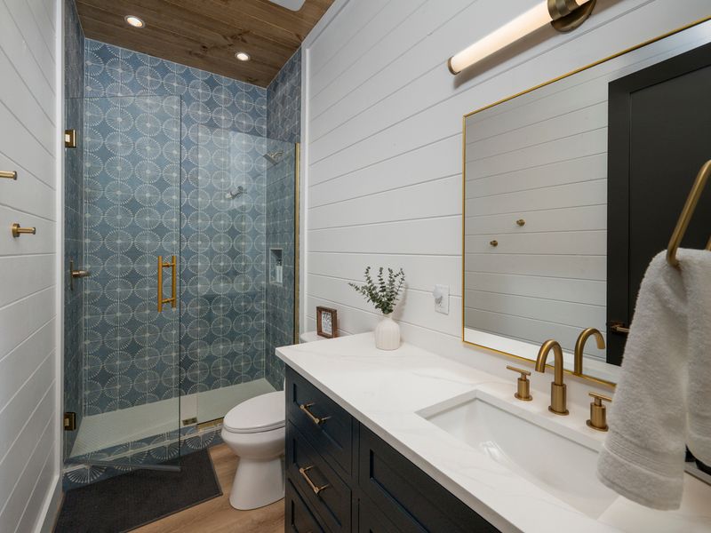 A beautiful bathroom features a striking blue-and-white patterned accent wall, elegant gold fixtures, and a custom vanity.