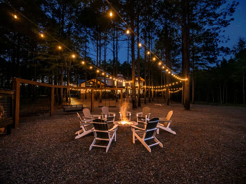 Cozy fire pit surrounded by white Adirondack chairs, illuminated by string lights in a serene