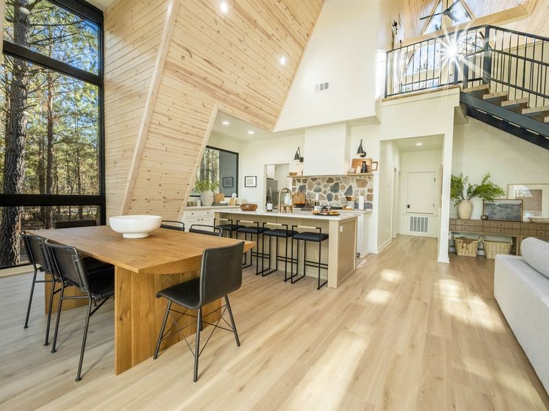 Sunlight pours through large windows, highlighting warm wood and modern design