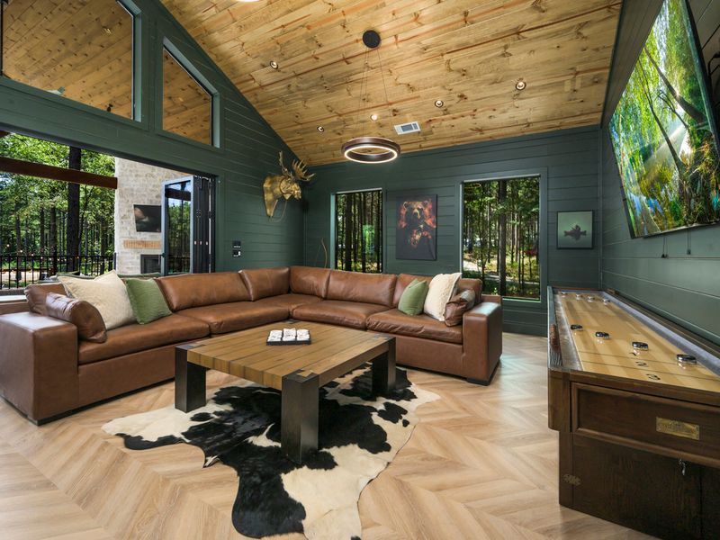 Relax in style in this beautifully designed game room, featuring a comfortable leather sectional, shuffleboard, and stunning views of the surrounding woods.