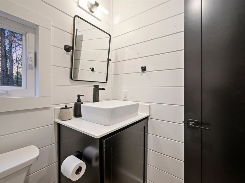 This stylish guest bathroom features modern finishes, a sleek vanity, and charming woodland views.