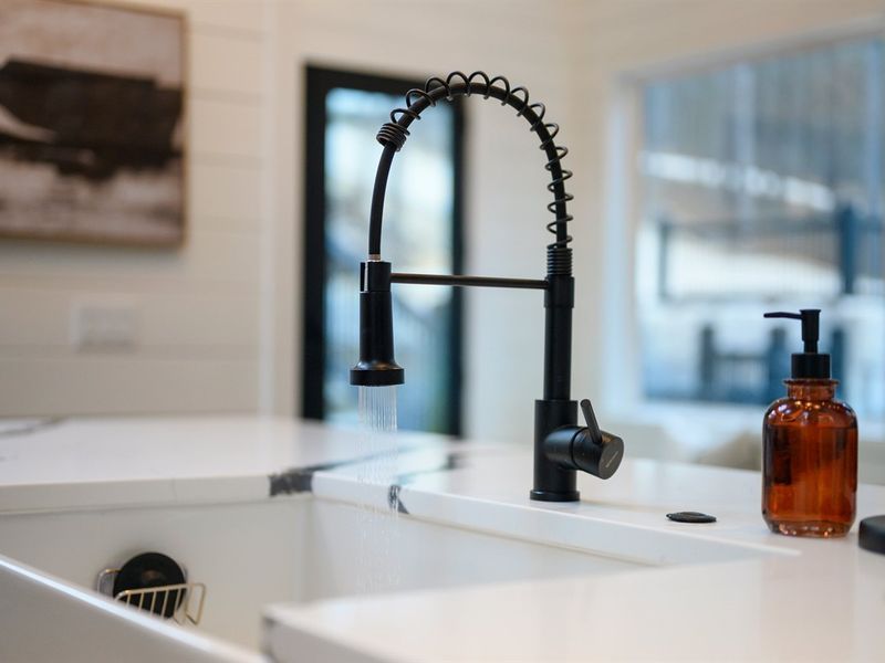 The oversized farmhouse sink with sleek black faucet makes cleanup easy while you enjoy peaceful forest views through the surrounding windows.