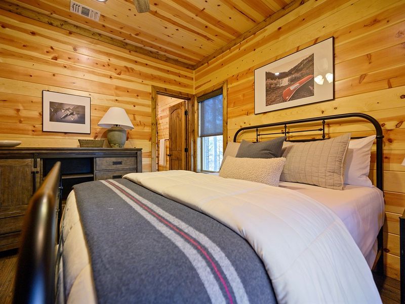 Cozy cabin interior featuring a comfortable bed with a striped blanket, wooden walls, and rustic