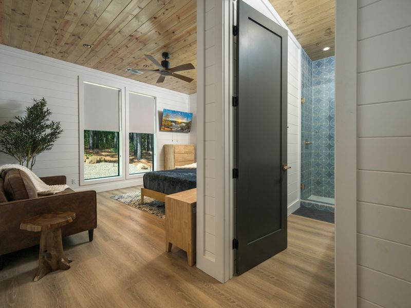 Bright and inviting bedroom with oversized windows, cozy seating, and natural wood accents.