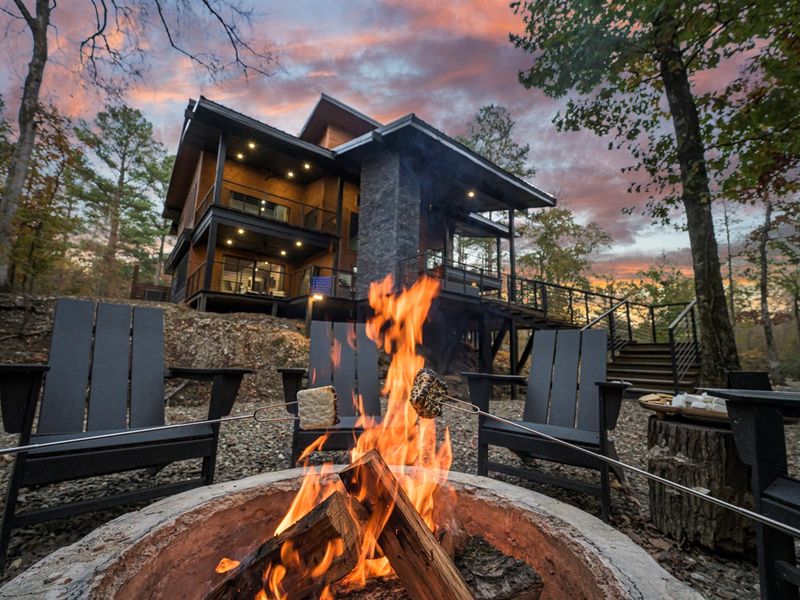 A perfect Broken Bow night: crackling fire, forest surroundings, and a beautifully lit cabin just behind you