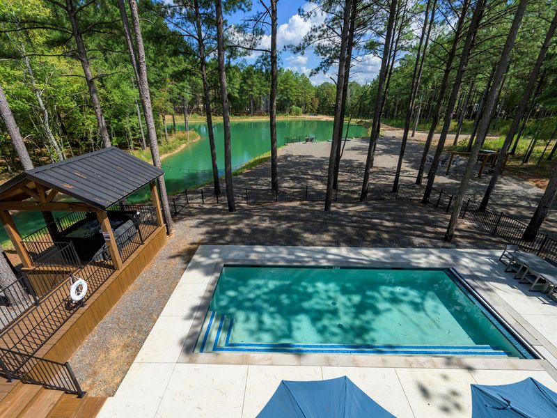 A stunning view captures the sparkling pool, private lake, and surrounding pine trees, creating a beautiful outdoor oasis for relaxing and enjoying the natural setting.