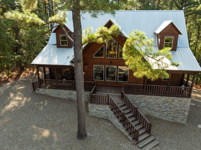 Cozy cabin exterior in a wooded setting, featuring a stone foundation, large windows