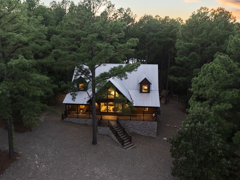Aerial view of a cozy cabin surrounded by tall pine trees, featuring a welcoming porch