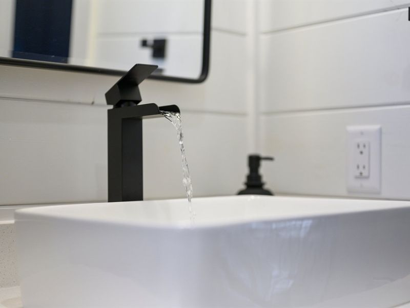 The guest bathroom features sleek black fixtures and crisp white shiplap for a clean, modern look.