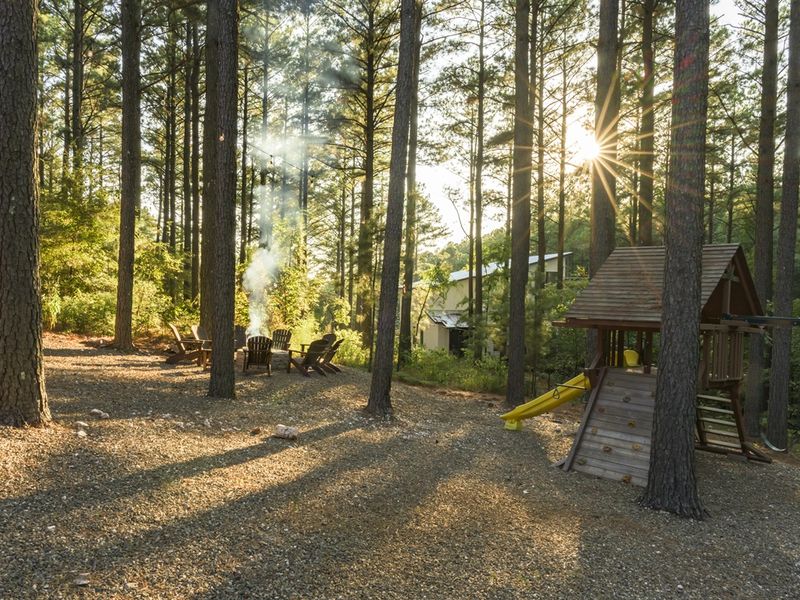 Cozy cabin retreat nestled among tall pine trees, featuring outdoor seating and a children's playset