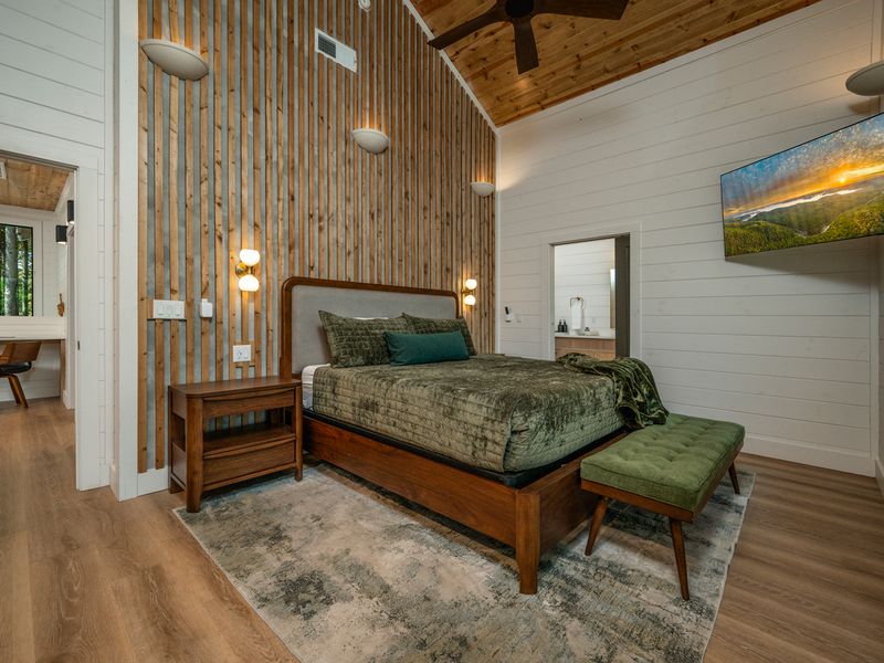 A cozy retreat features a beautifully crafted wood bed, layered green textiles, and a striking slatted wood accent wall beneath a warm wood ceiling.