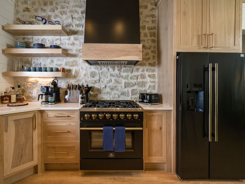 Stylish kitchen featuring a deluxe range, stone backsplash, natural wood cabinetry, and modern appliances, designed