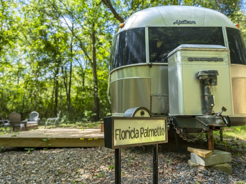 Airstream trailer named "Florida Palmetto" situated in a wooded area, with a wooden deck