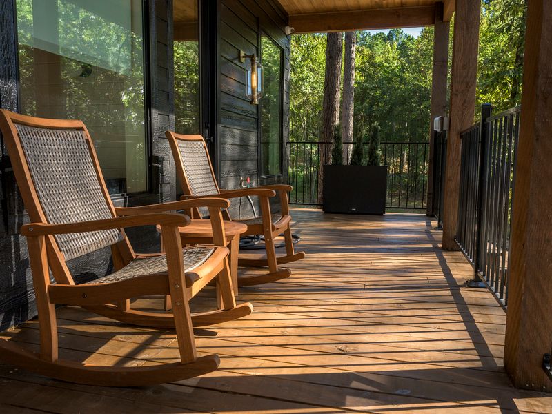 Wooden rocking chairs sit on the spacious covered deck of a luxury cabin, overlooking