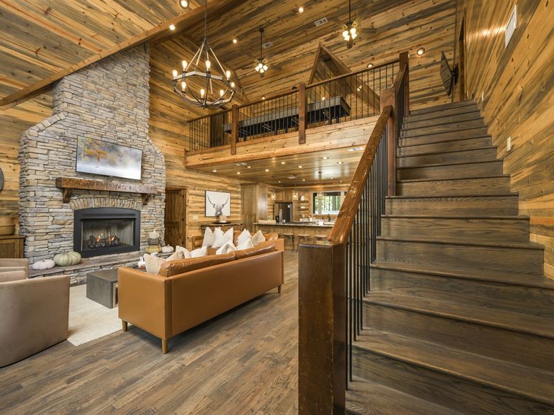 Cozy cabin interior featuring a stone fireplace, wooden beams, and a staircase, ideal for relaxing
