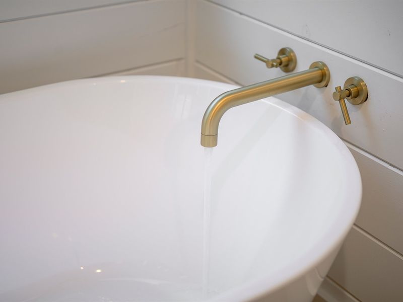 The elegant brushed brass tub filler adds a warm, modern touch to the freestanding soaking tub.