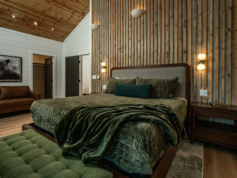 The beautifully layered bed takes center stage against the dramatic wood-slat wall, with warm lighting and an adjoining bath adding to the sense of comfort.