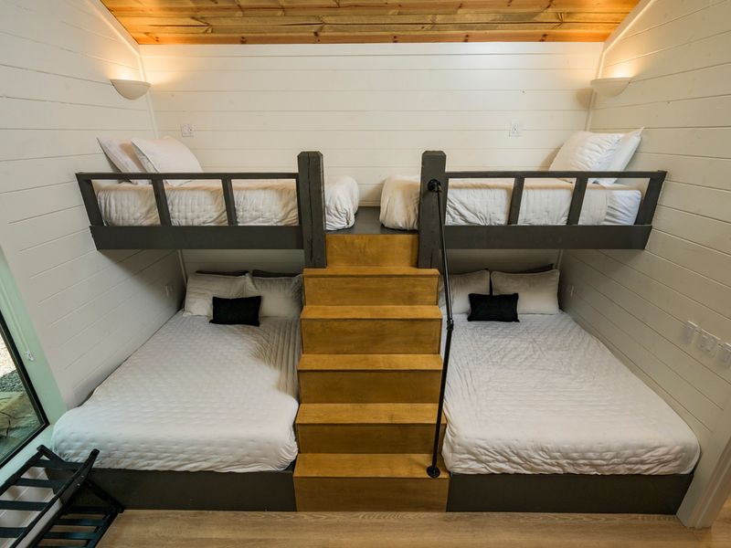 A charming view of the loft sleeping area showcases the rustic staircase, wood flooring, and four inviting beds.