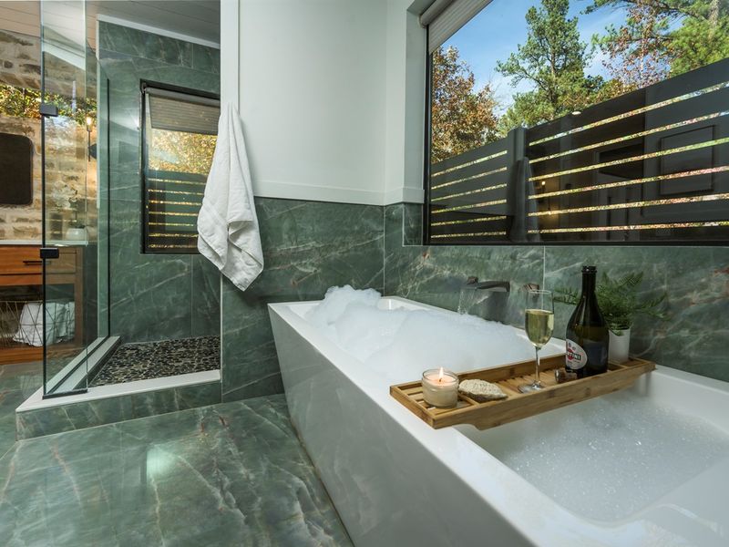 Relax, soak, and slow down — this luxury bathroom features a deep tub, walk-in shower, and serene forest backdrop