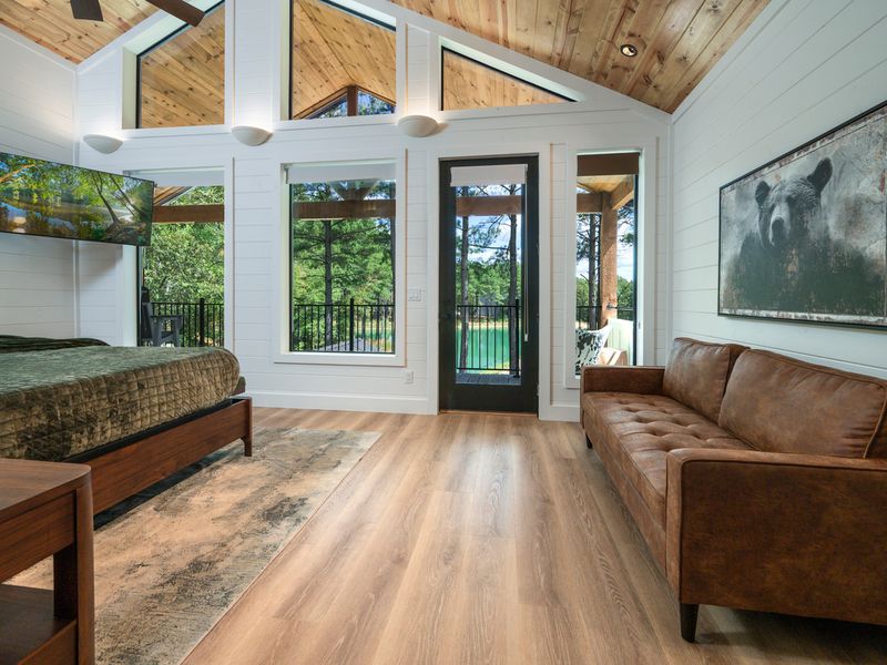 A serene primary bedroom blends warm wood, rich green bedding, and expansive windows that bring the beauty of the surrounding forest indoors.