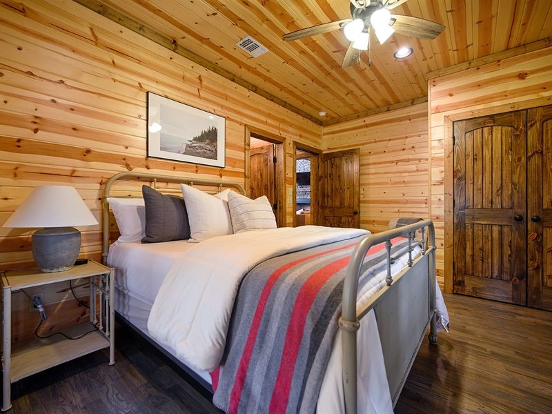 Cozy cabin bedroom interior with a wooden bed frame, lamp, and rustic decor, offering comfort