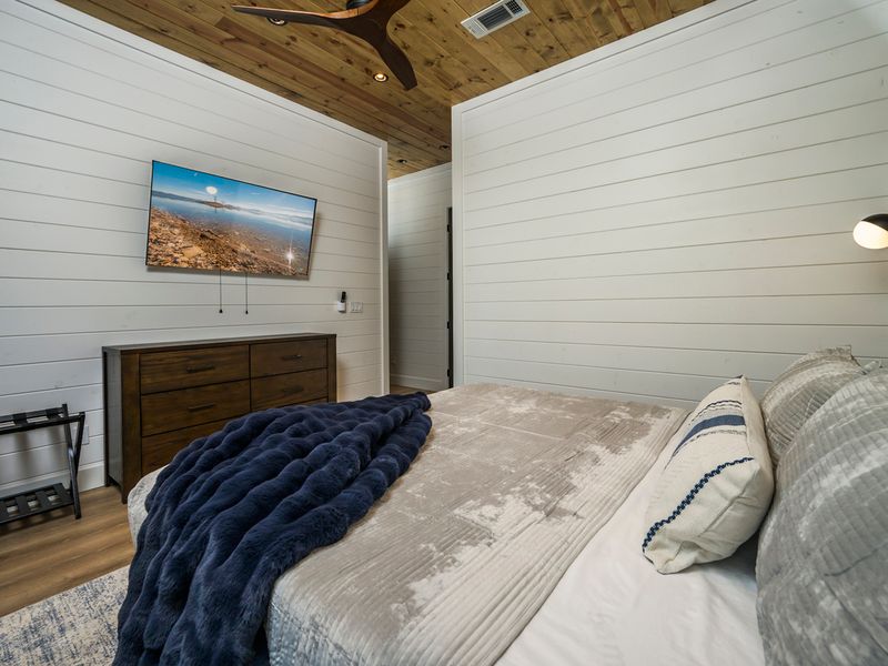 A beautifully appointed bedroom with a comfortable bed, cozy textures, and a warm wood ceiling.