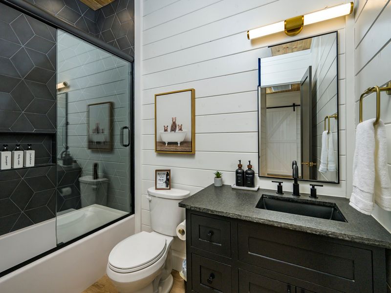 A beautifully appointed bathroom combines crisp white shiplap, dramatic charcoal tile, and warm brass accents for a sophisticated yet inviting retreat.