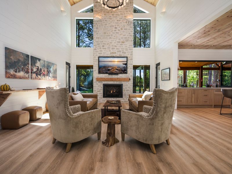 The spacious great room combines soaring ceilings, a striking stone fireplace, comfortable furnishings, and expansive windows for the perfect place to gather and unwind.