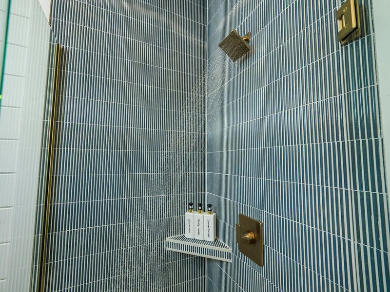 Step into a luxurious walk-in shower with floor-to-ceiling tile, rainfall showerhead, and a convenient built-in niche stocked with shampoo, conditioner, and body wash.