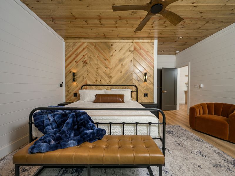 A beautifully styled bedroom features a comfortable bed, warm wood chevron accent wall, cozy seating, and rich blue and caramel accents for a relaxing retreat.