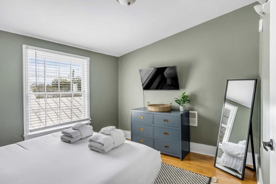 Bedroom 2: Bright queen bedroom with a TV and oversized windows.