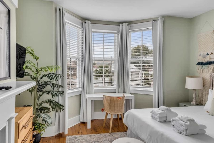 A grand primary retreat with a decorative fireplace, workspace, TV, and sun-filled windows.