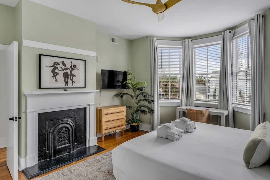 A grand primary retreat with a decorative fireplace, workspace, TV, and sun-filled windows.