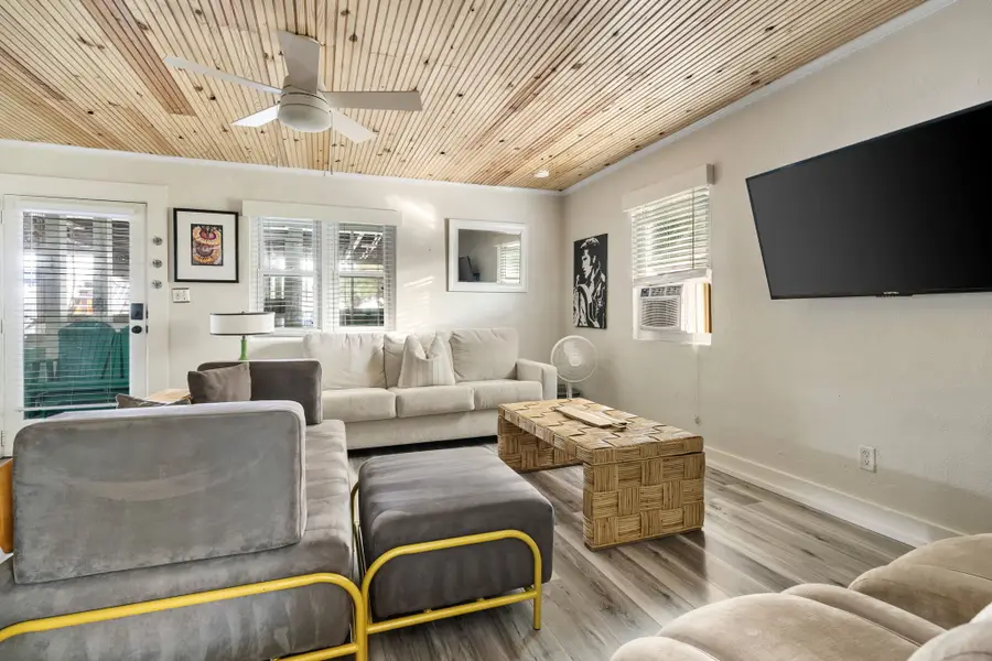 Gather in the bright and spacious living room, featuring cozy seating, a large TV, and walls of windows that fill the space with natural light.