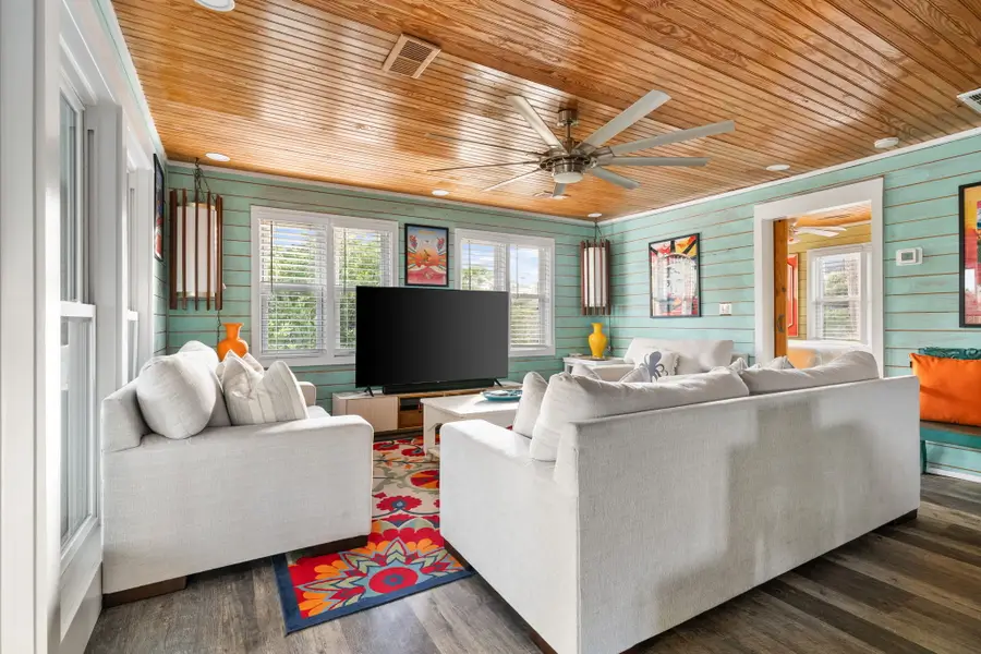 Gather in the bright and spacious living room, featuring cozy seating, a large TV, and walls of windows that fill the space with natural light.