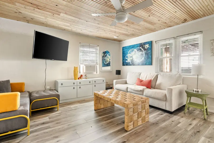 Gather in the bright and spacious living room, featuring cozy seating, a large TV, and walls of windows that fill the space with natural light.